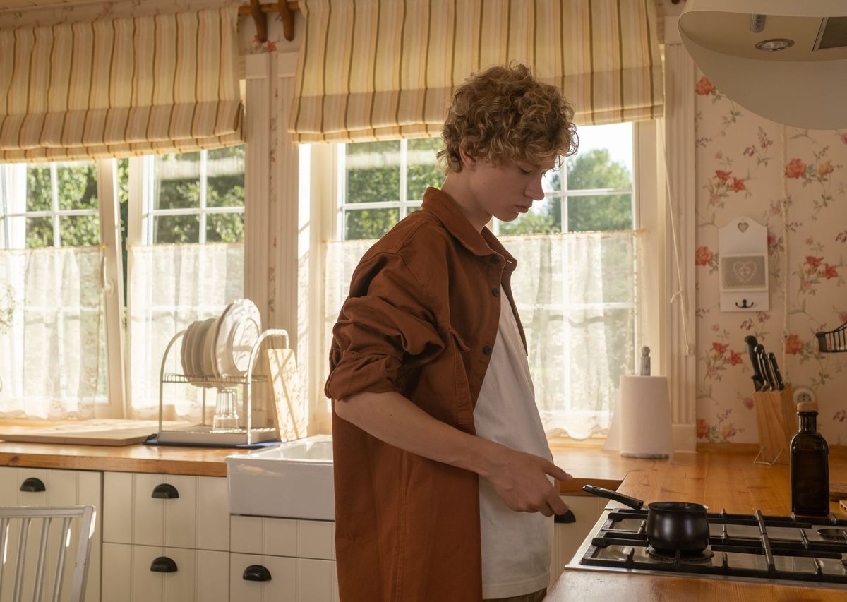 Een jongen staat in een zonnige keuken zelf te koken